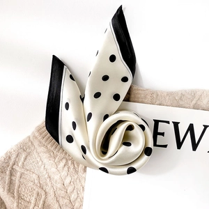 Classic black and white polka dot silk scarf draped on a cozy beige knitted sweater