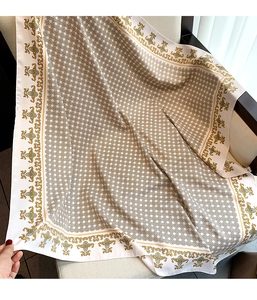 Close-up of beige silk scarf with geometric patterns and golden floral motifs on a chair
