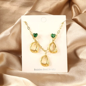 Detail of stainless steel jewelry set with green heart stones on champagne silk