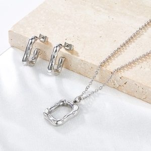 Modern silver geometric jewelry set with earrings and necklace on travertine stone