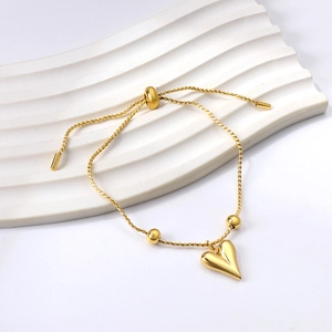 Gold stainless steel bracelet with 3D heart charm and sliding gold beads on white background