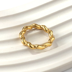 Bague torsadée en acier inoxydable doré poli avec détails perlés sur fond blanc épuré