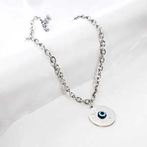 Gros plan d'un collier en argent avec pendentif œil protecteur sur un tissu texturé blanc