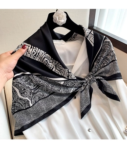 Detail of a black and white geometric silk scarf tied on a white shirt with hand display