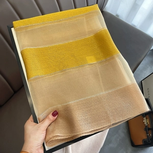 Detail view of yellow and champagne striped sheer silk blend scarf held over a leather sofa