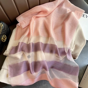 Detail of pink and purple striped silk blend scarf draped over a beige coat and leather sofa