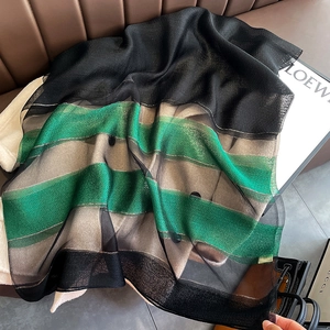 Detail of color-block silk blend scarf in black, green, and beige on leather sofa