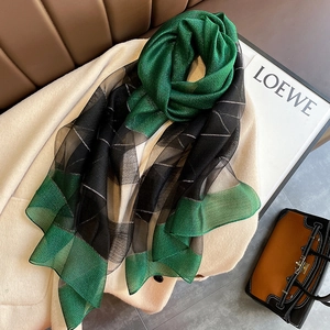 Detail of green and black silk blend scarf with silver lurex grid on beige coat