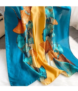 Detailed close-up of silk scarf featuring elegant blue and orange ginkgo leaf patterns