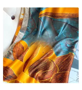 Détail de l'écharpe en soie turquoise et orange avec motifs de feuilles dorées sur cuir
