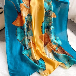 Blue and yellow silk-feel scarf with golden ginkgo leaves on white plush background
