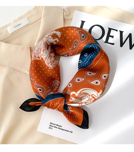 Detailed view of orange and navy paisley silk scarf knotted on a beige collared shirt