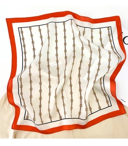 Close-up of silk square scarf with orange borders and golden chain patterns on fabric