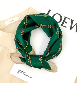 Close-up of emerald silk scarf with golden buckle print on beige shirt background