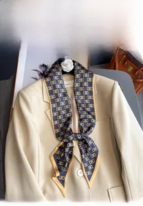 Foulard en soie bleu marine à motif monogramme et camélia blanc sur un blazer beige