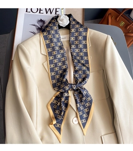 Détail d'un foulard en soie avec logo doré stylisé sur un blazer beige et magazine de luxe