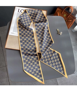 Détail d'un foulard twilly bleu marine avec bordures jaunes et logo sur sac en cuir