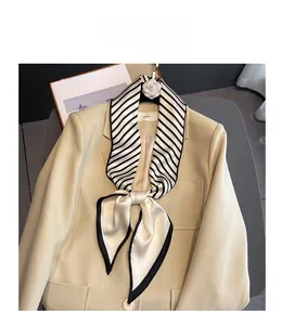 Detail of black and white striped silk scarf styled on a beige blazer with flower brooch