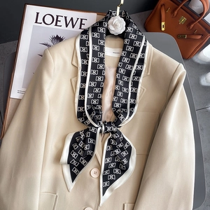 Foulard en soie à motif géométrique noir et blanc stylisé sur un blazer de couleur claire