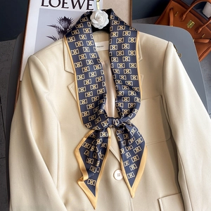 Foulard en soie bleu marine à motifs dorés porté sur le col d'un blazer beige