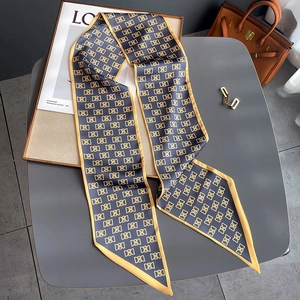 Foulard en soie bleu marine à motifs géométriques dorés à côté d'un sac à main en cuir