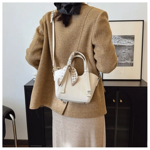 Detail of off-white lychee leather bucket bag with silk scarf handle on a model