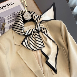 Elegant black and white striped satin scarf styled as a bow on a beige blazer collar