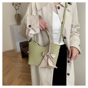 Pale green pebble leather bucket bag with pink plaid scarf detail on beige trench coat