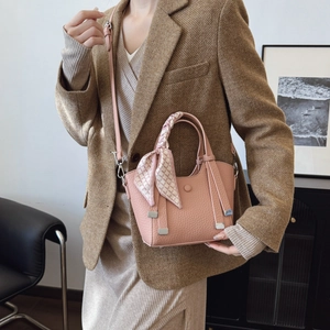 Pink lychee texture bucket bag with silk scarf handle worn by a model in a brown suit