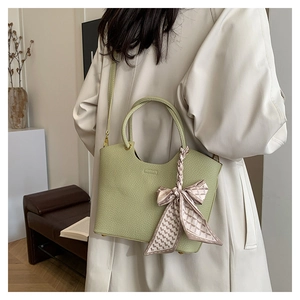 Detail of avocado green leather bucket bag with decorative silk scarf on coat-clad model
