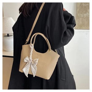 Close-up of light brown leather bucket bag featuring decorative silk scarf on the handle