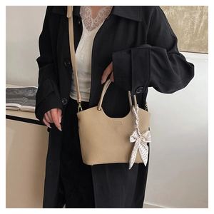 Close-up of beige pebble leather bucket bag with decorative silk scarf and adjustable strap