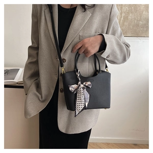 Detail of black lychee grain leather bucket bag with geometric silk scarf on handle