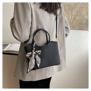 Detail of black lychee grain bucket bag with decorative printed silk scarf on the handle