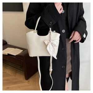 Detail of cream pebbled leather handbag with decorative checkerboard bow and U-shaped top