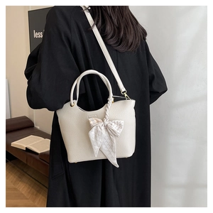 Detail view of cream leather bucket bag with plaid scarf bow and gold hardware on model