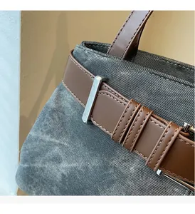 Detail van vintage grijze denim handtas met bruine leren riem en zilveren metalen gesp