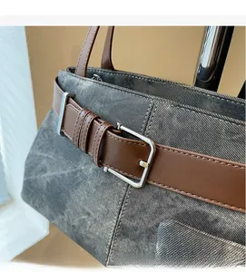 Detail van grijze denim tas met bruine kunstleren riem en een zilverkleurige metalen gesp