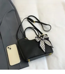 Detailed top view of black pebbled leather bucket bag with bow and phone for scale