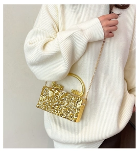 Dettaglio della borsa clutch dorata con manici a drago e texture metallo liquido su maglione