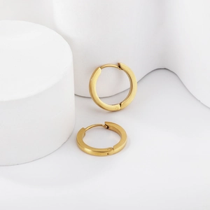 Boucles d'oreilles créoles minimalistes en acier doré mat sur fond blanc géométrique