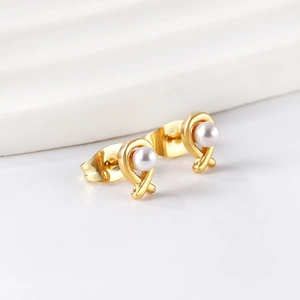 Close-up of golden cross knot earrings with white pearls on a textured background