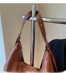 Detail of adjustable leather shoulder strap with silver metal eyelets on a brown hobo bag