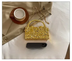 Clutch dorata con trama a crepe, manici a drago e catena accanto a uno smartphone