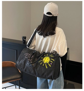 Large black canvas travel bag with sunflower print shown worn by a model in casual setting