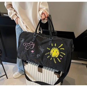 Detailed view of black canvas travel bag with sunflower graffiti on a white suitcase