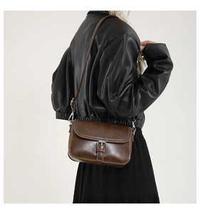 Sac bandoulière vintage en similicuir marron avec surpiqûres blanches porté par un modèle