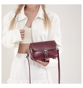 Sac bandoulière rouge foncé avec boucle argentée porté par un mannequin sur fond blanc