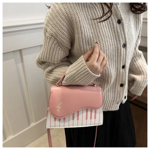 Détail d'un sac bandoulière rose et blanc avec motif touches de piano et clé de sol dorée