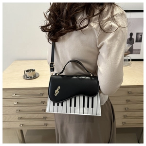 Dettaglio borsa motivo tastiera pianoforte con chiusura a nota dorata su outfit sobrio